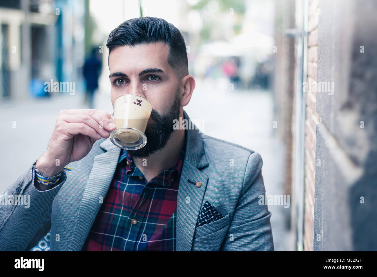 Giovani hipster sorseggiando un cappuccino sulla street cafe terrazza. Elegante modello maschio avente tazza di caffè nella città. Ben vestito uomo godendo espresso Foto Stock