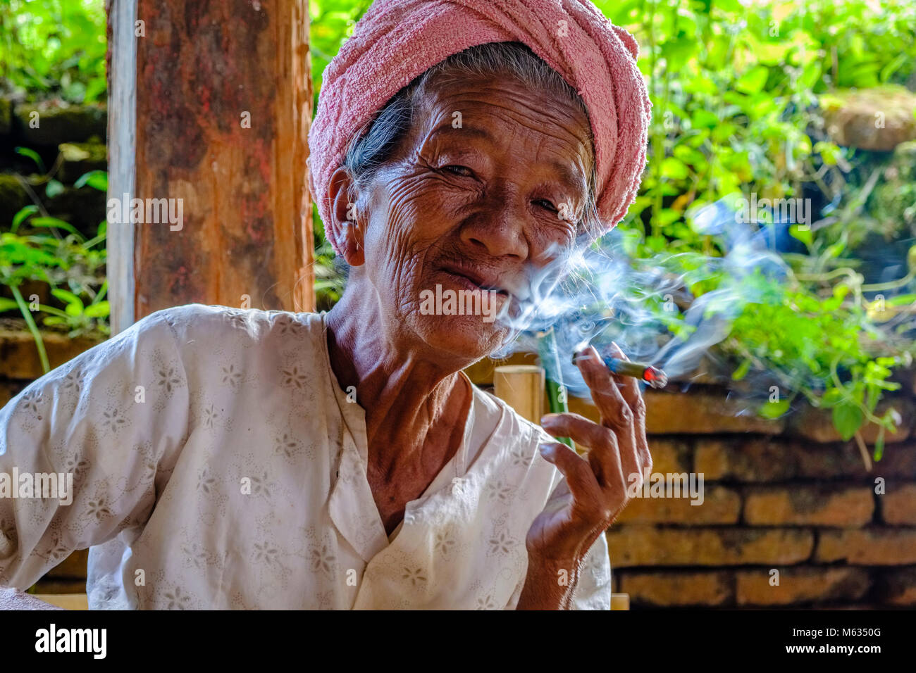 Una donna anziana sta fumando una Cheerot, un sigaro locale, nel villaggio di Indein vicino al Lago Inle Foto Stock