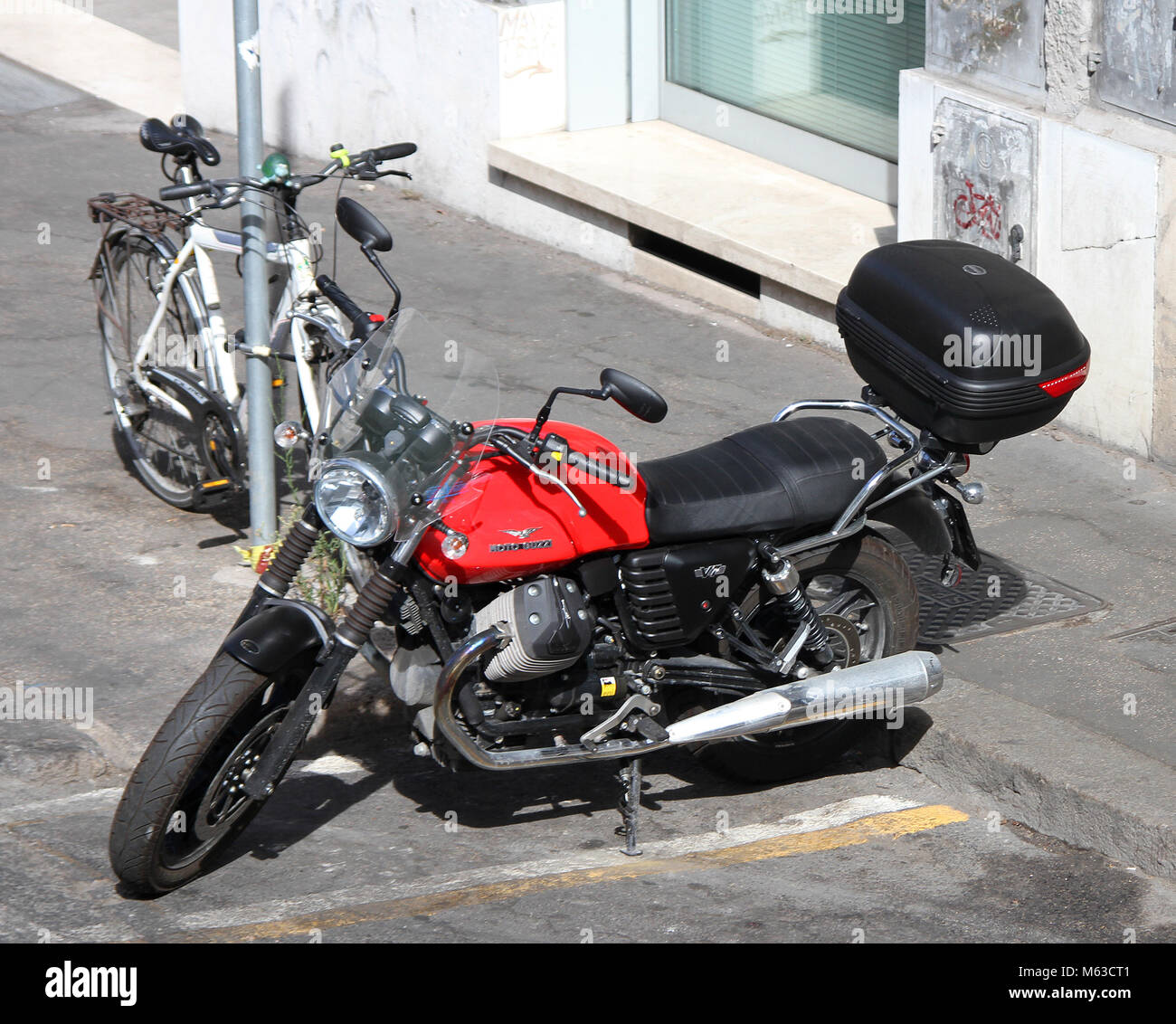 Un rosso Moto Guzzi V7 parcheggiato a fianco di una bicicletta fissata contro un segno posto, Roma, Italia. Foto Stock