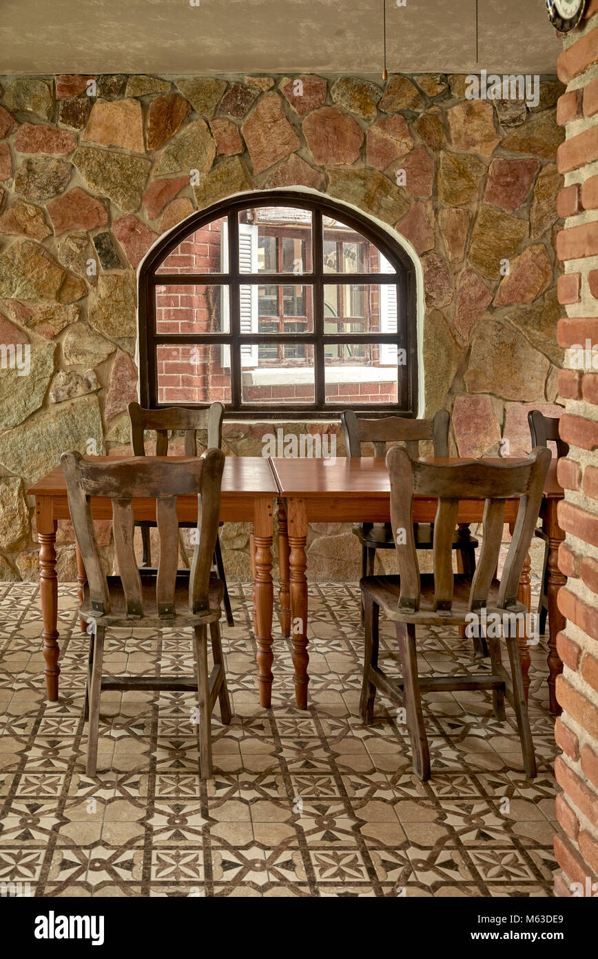 Interno rustico in pietra con tavoli e sedie in legno. Interni del ristorante Vintage con un'accogliente sala da pranzo ad angolo. Foto Stock