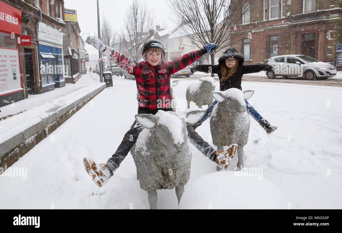 Lockerbie, Scotland, Regno Unito. 28 Feb, 2018. Regno Unito Meteo. Neve pesante provoca red alert in parti della Scozia. La neve che cade su di Lockerbie. Conor e Lucy Walker seduti sulla pecora sculture a Lockerbie Town Center. Scotland Credit: Allan Devlin/Alamy Live News Foto Stock