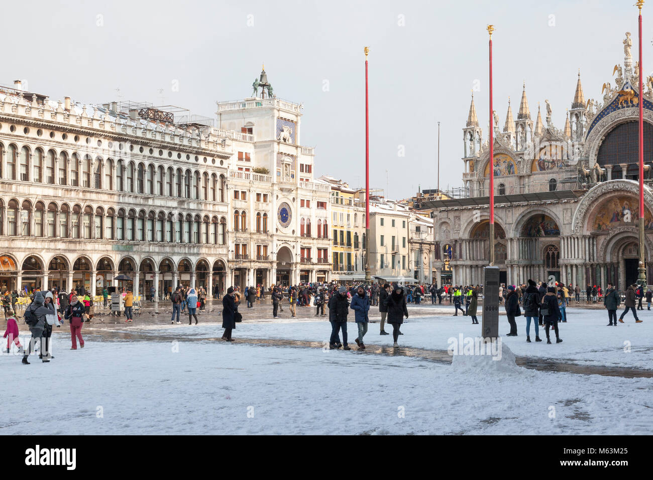Venezia, Veneto, Italia, 28 Fenbruary 2018. Raro neve a Venezia causata dal clima Siberiano spazzamento anteriore Europa, i turisti a piedi nella neve in Piazza San Marco di fronte della Basilica di San Marco e la Torre dell Orologio. Foto Stock