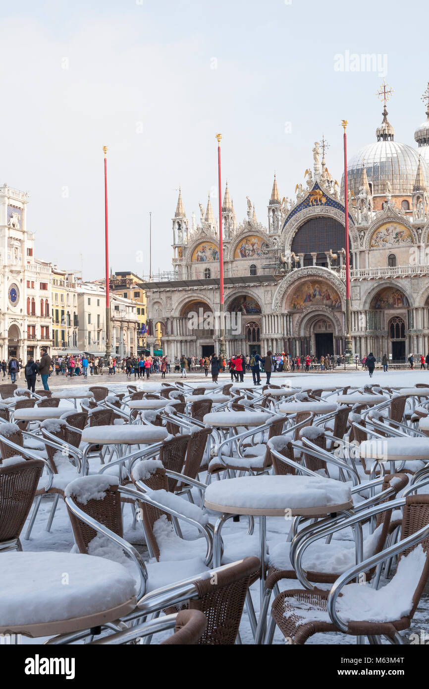 Venezia, Veneto, Italia, 28 Fenbruary 2018. Raro neve a Venezia causata dal clima Siberiano spazzamento anteriore Europa, coperta di neve i tavoli e le sedie in Piazza San Marco con i turisti in background di fronte alla Torre dell Orologio e la Basilica di San Marco e Basilica di San Marco. Foto Stock