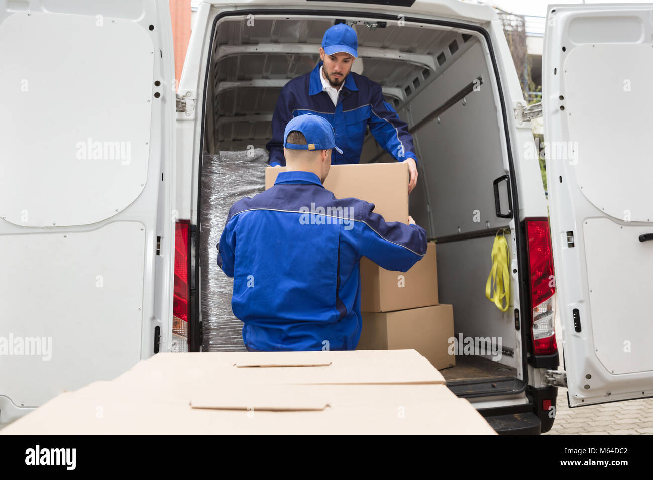 Due giovani maschi Movers trasportare la scatola di cartone dal carrello Foto Stock