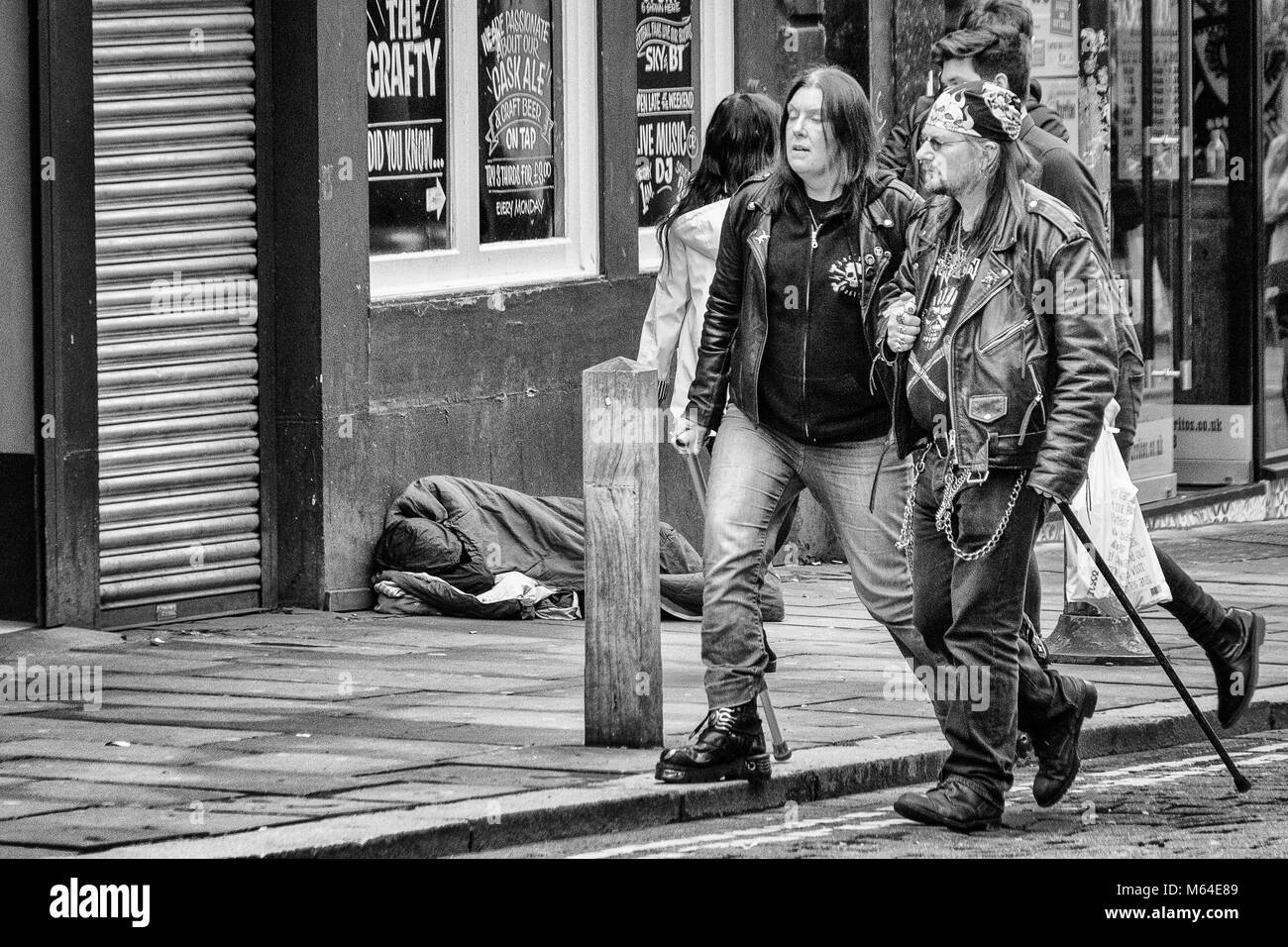 La mezza età punk giovane camminando in Liverpool con la persona senza dimora addormentato in un negozio porta in background Foto Stock