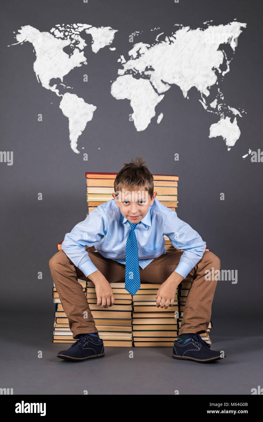 Il concetto di istruzione. La mappa del mondo dietro un allegro ragazzo seduto su un trono di libri Foto Stock
