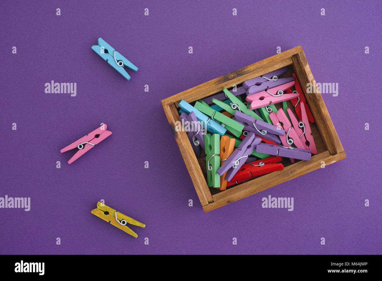 Clothespins colorati in una scatola di legno su sfondo viola. Close up. Foto Stock