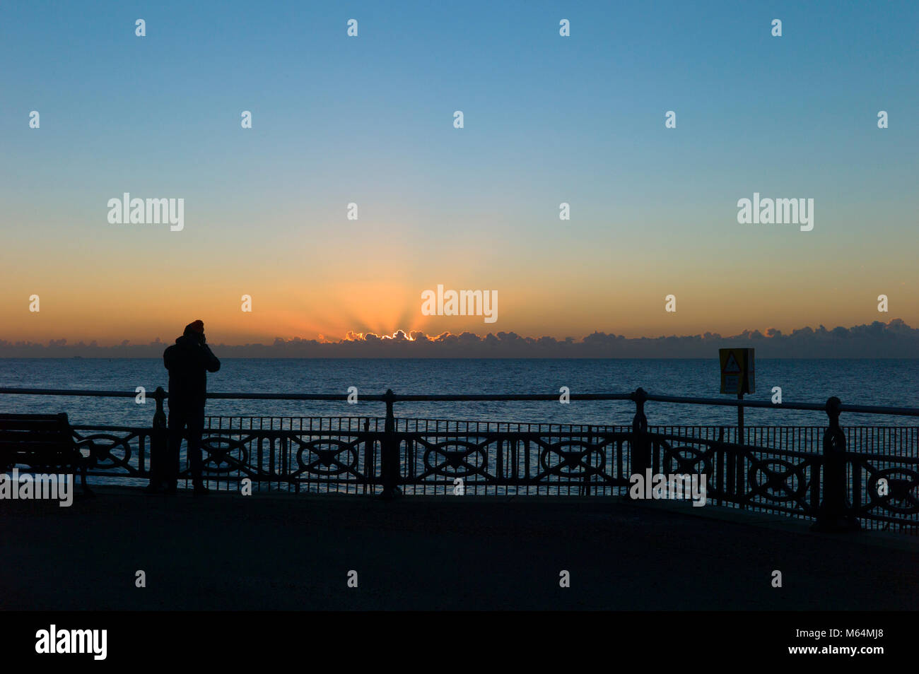 Persona in silhouette in riva al mare a fotografare le ringhiere sunrise Foto Stock