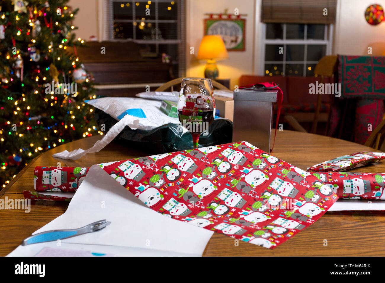 Un bicchiere di vino rosso sito nelle vicinanze di Natale carta di avvolgimento in un salotto con un albero di Natale in background Foto Stock