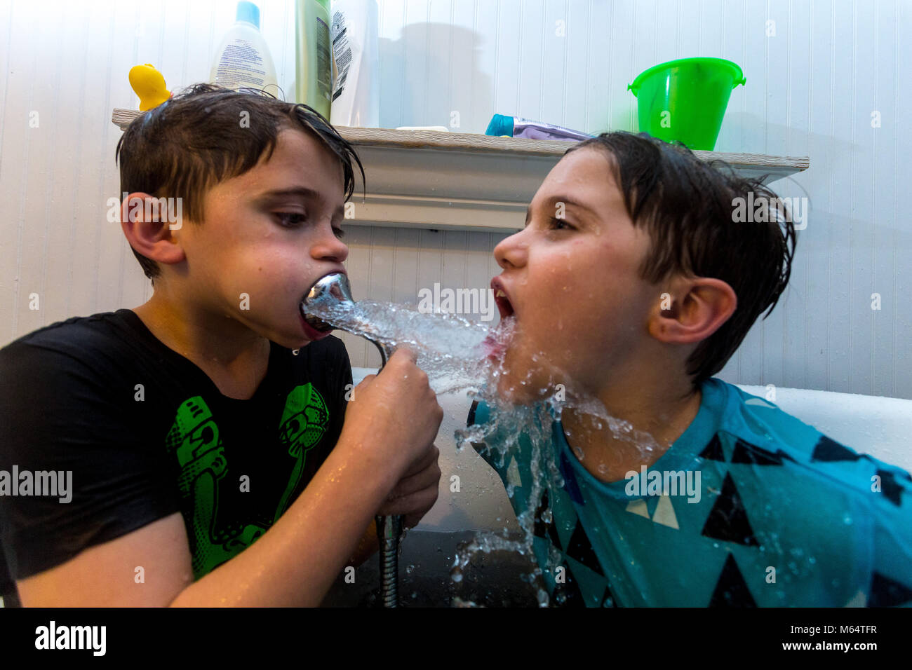 Twin fratelli caucasici giocare nella loro acqua riempito la vasca insieme con i loro vestiti su Foto Stock