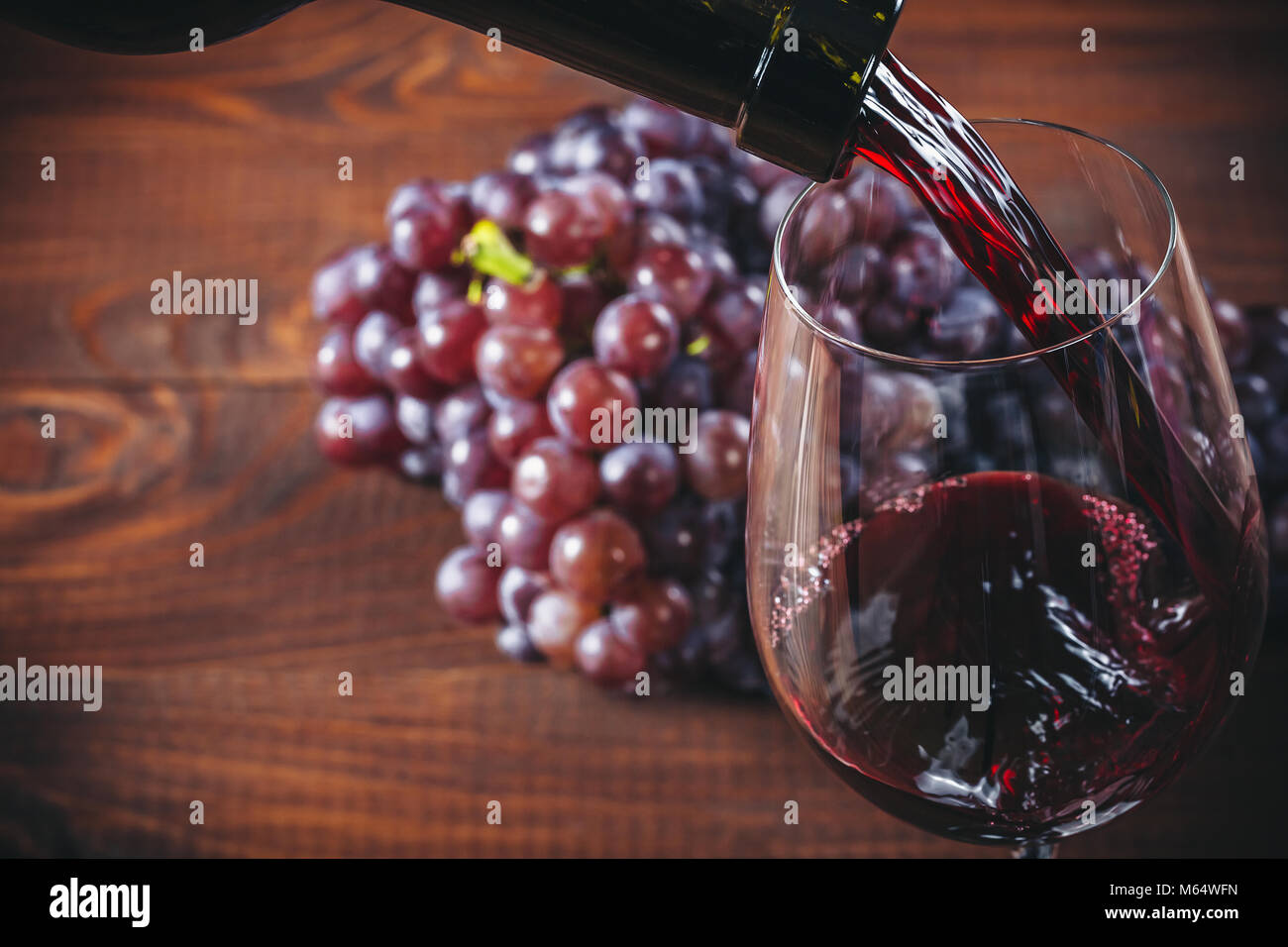 Bottiglia e bicchiere di vino rosso, uva e sughero su sfondo di legno. Foto Stock