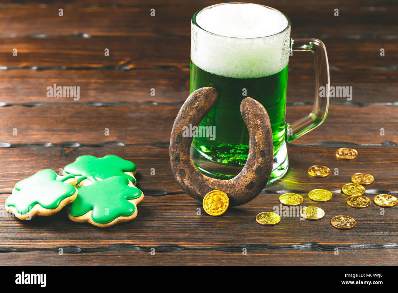 Patrick's Day lo sfondo con un bicchiere di birra verde trifoglio e il ferro di cavallo e pan di zenzero con monete d oro su sfondo di legno Foto Stock