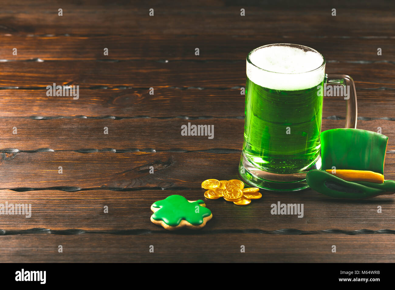 Patrick's Day lo sfondo con un bicchiere di birra verde e trifoglio gingerbread con monete d oro su sfondo di legno Foto Stock