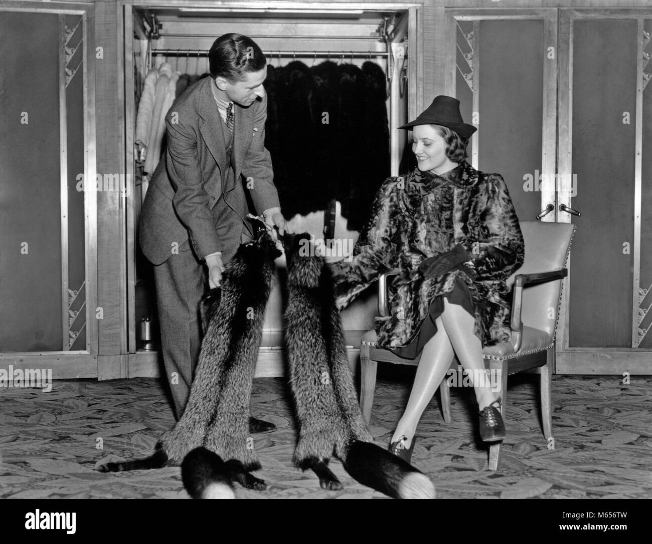 Negli anni trenta la donna nel salone di pelliccia che indossa PELLICCIA  seduto mentre il venditore mostra la sua pelliccia di volpe stole - f8344  HAR001 HARS vecchia industria tempo OLD FASHION