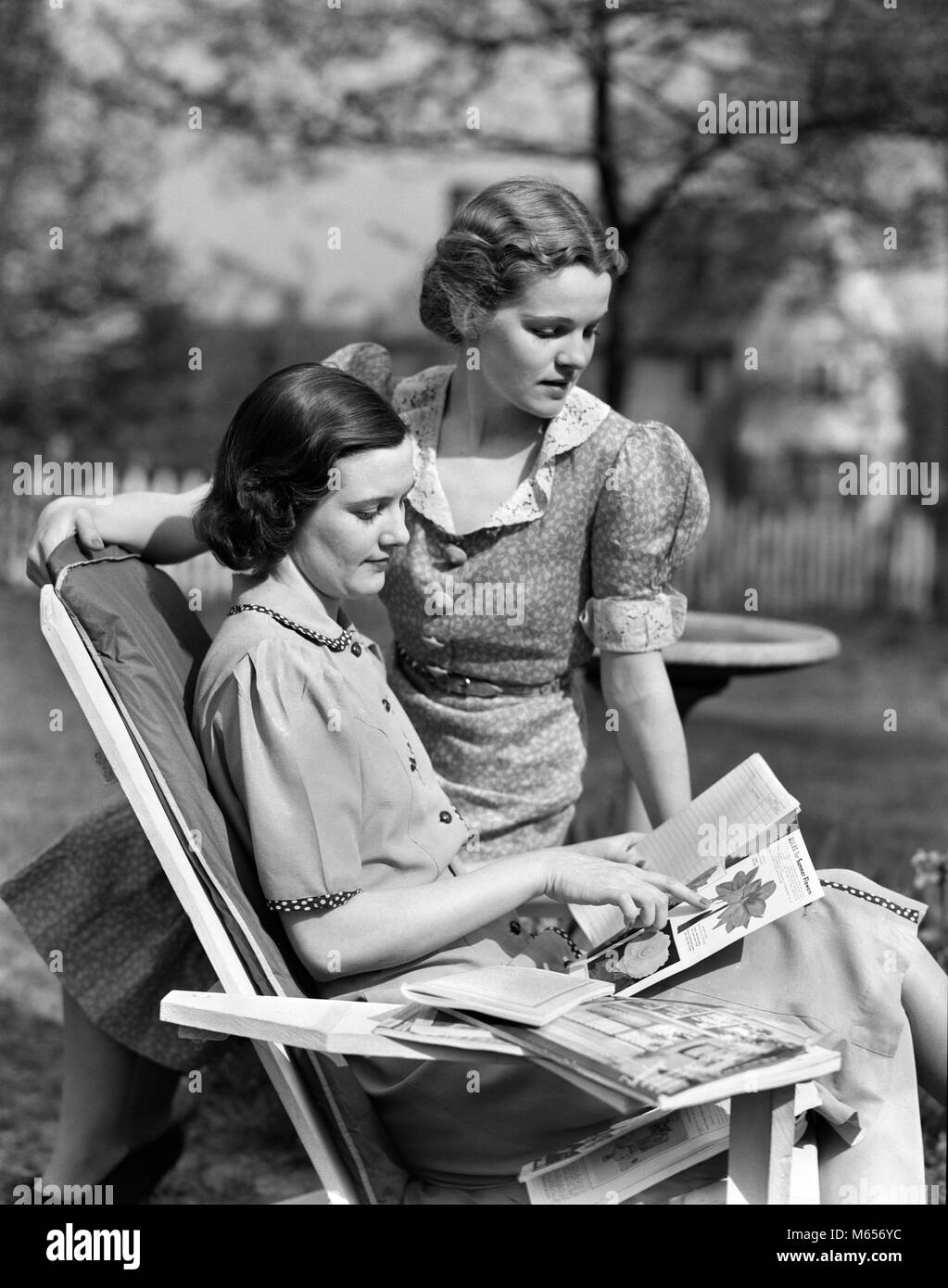 Negli anni Trenta due donne nel cortile uno seduto nella sedia prato altri guardando sopra la spalla la lettura di semi vegetali CATALOGHI - g4458 HAR001 HARS CAUCASIAN LIFESTYLE femmine cresciuto HOME VITA spazio copia amicizia a mezza lunghezza LADIES CRESCIUTI I fratelli sorelle nostalgia convivere 20-25 anni BRUNETTE sogni scelta relax ricreazione 18-19 anni di crescita gemelli di Sementi prato cooperazione sedia metà donna adulta giovane donna adulta B&W in bianco e nero di cataloghi etnia caucasica scegliendo in vecchio stile persone Foto Stock