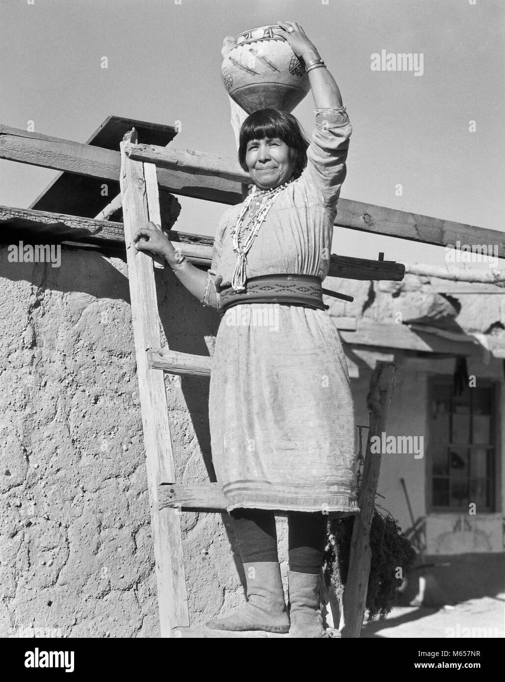 1930s Native American Indian donna in piedi sulla scaletta olla di contenimento acqua Vaso in ceramica SUL SUO CAPO COCHITI PUEBLO NEL NUOVO MESSICO USA - MI1694 HAR001 HARS INDIANI DEGLI STATI UNITI D'AMERICA NOSTALGIA in ceramica di mezza età JAR il contatto visivo 40-45 anni 45-50 anni oggetto singolo donna di mezza età cordone orgoglio nativo americano COCHITI PUEBLO nativi americani Messico Nuovo B&W IN BIANCO E NERO guardando la fotocamera in vecchio stile OLLA PERSONE Foto Stock