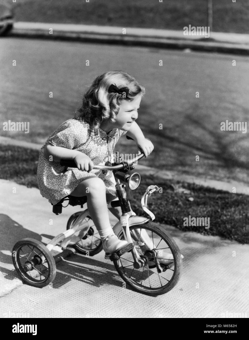 1930s 1940s ragazza triciclo di equitazione sul marciapiede - J8116 HAR001 HARS BIKES 3-4 anni la felicità di triciclo elevato angolo emozione ricreazione novellame pedalando TRIKE B&W in bianco e nero di etnia caucasica DEMON di vecchio stile Foto Stock