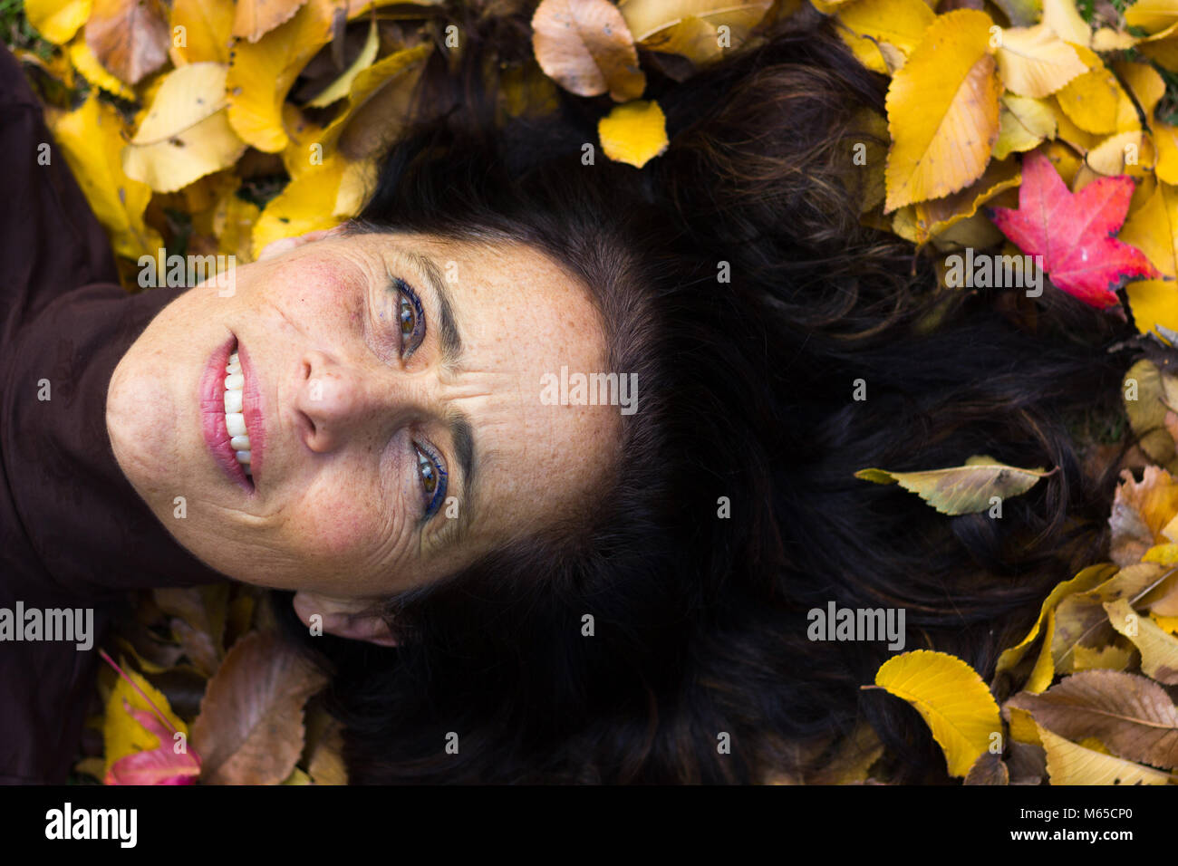 Incantevole donna matura ritratto sensazione confortevole giacente su un terreno pieno di giallo e marrone lascia nel parco durante la stagione autunnale. Concetto visionario Foto Stock