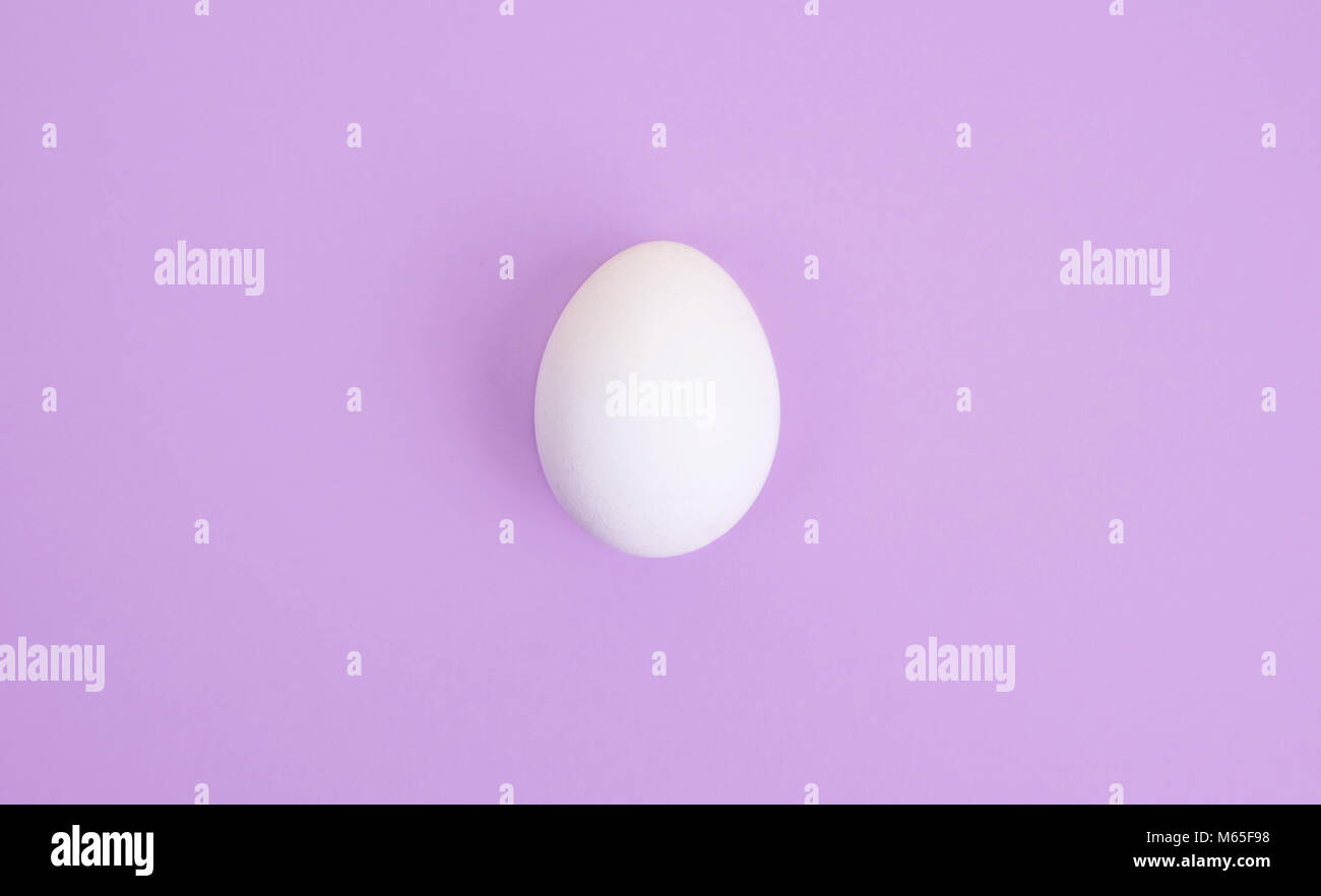Un uovo bianco pastello su sfondo lilla. Foto Stock