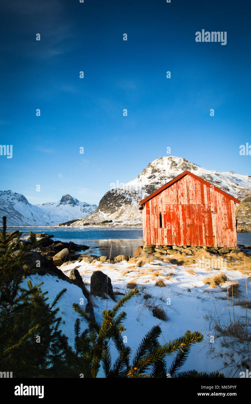 Capanna di rosso con un piccolo abete in prossimità di acqua e montagne Foto Stock