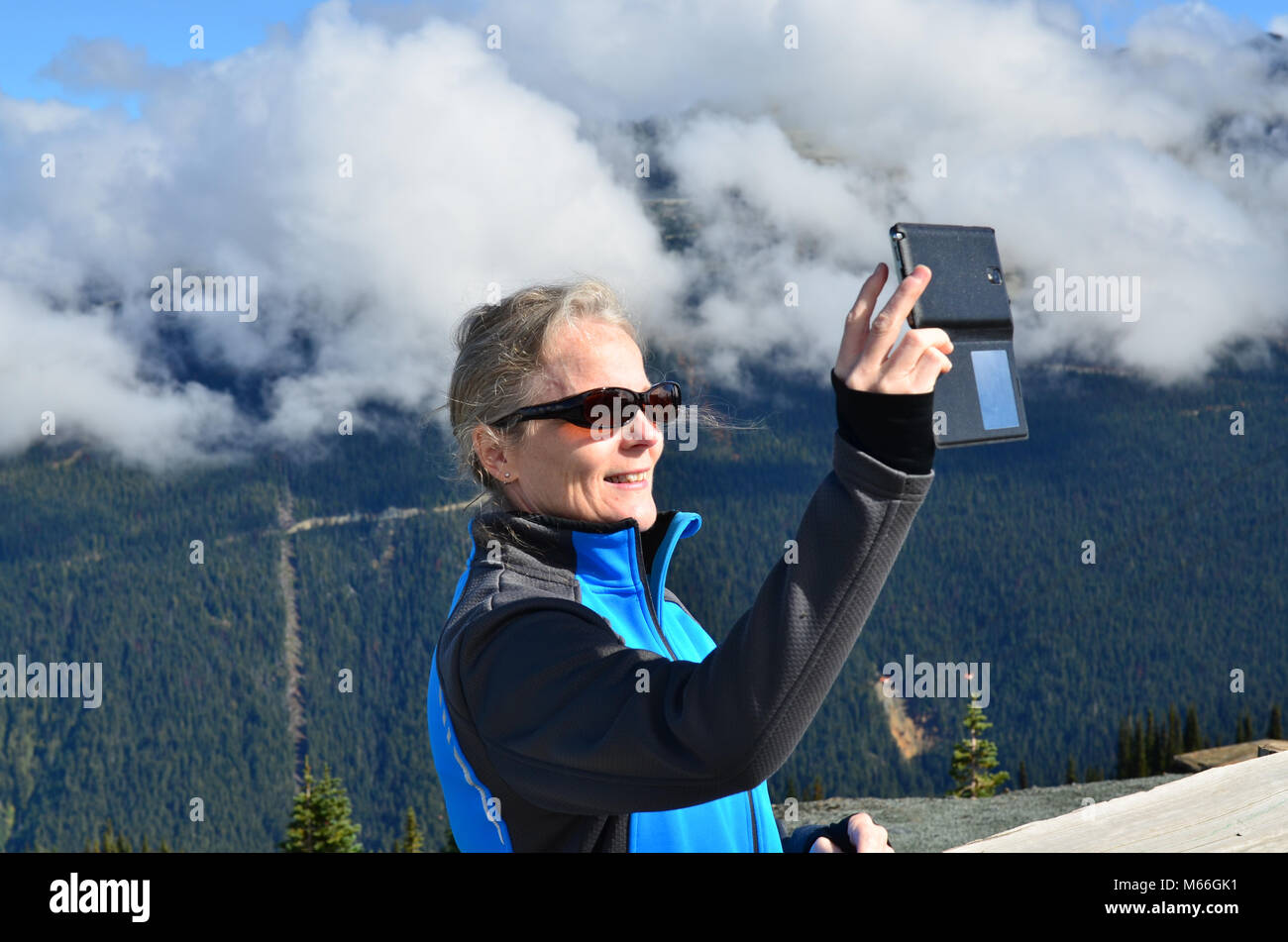 Donna in piedi su una montagna che prende un selfie, Whistler, Columbia Britannica, Canada Foto Stock