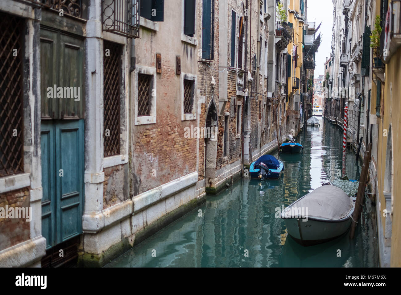 Canali d'acqua a Venezia con barca in movimento, nessuna folla e nessuna persona identificabile durante l'inverno e cieli bianchi limpidi. Foto Stock