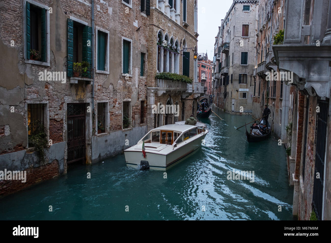Canali d'acqua a Venezia con barca in movimento, nessuna folla e nessuna persona identificabile durante l'inverno e cieli bianchi limpidi. Foto Stock