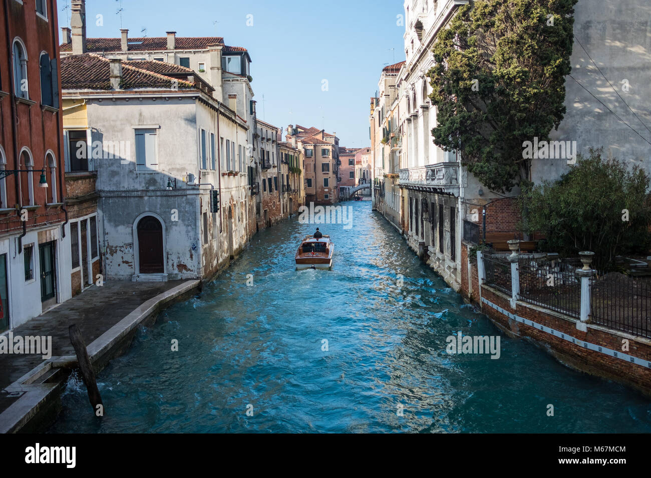 Canali d'acqua a Venezia con barca in movimento, nessuna folla e nessuna persona identificabile durante l'inverno e cieli bianchi limpidi. Foto Stock