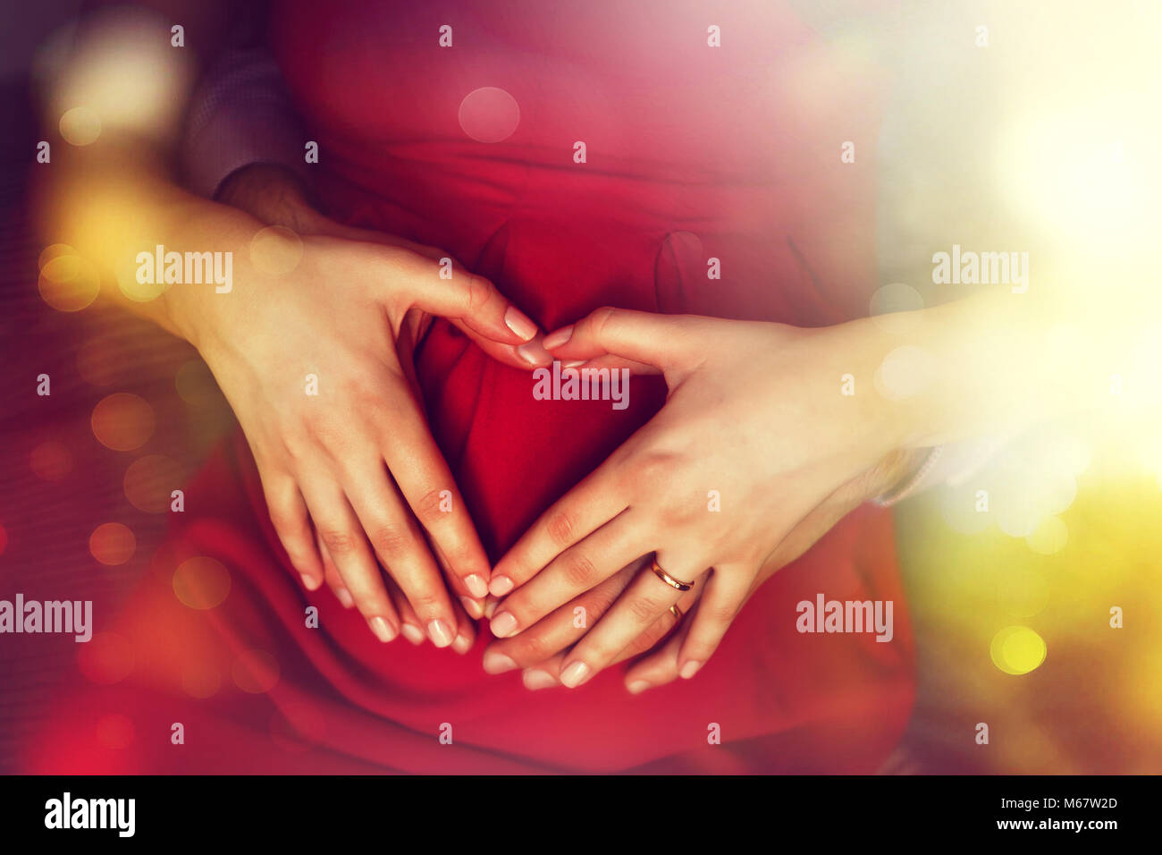 La gravidanza e la famiglia il concetto di amore. Aspettando i genitori di contenimento a forma di cuore le mani sulla pancia Foto Stock