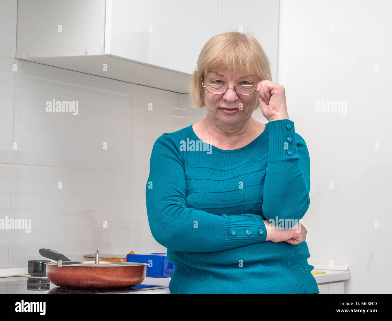 Caucasian donna di mezza età guardando la fotocamera su occhiali, in piedi in cucina vicino slove con padella Foto Stock
