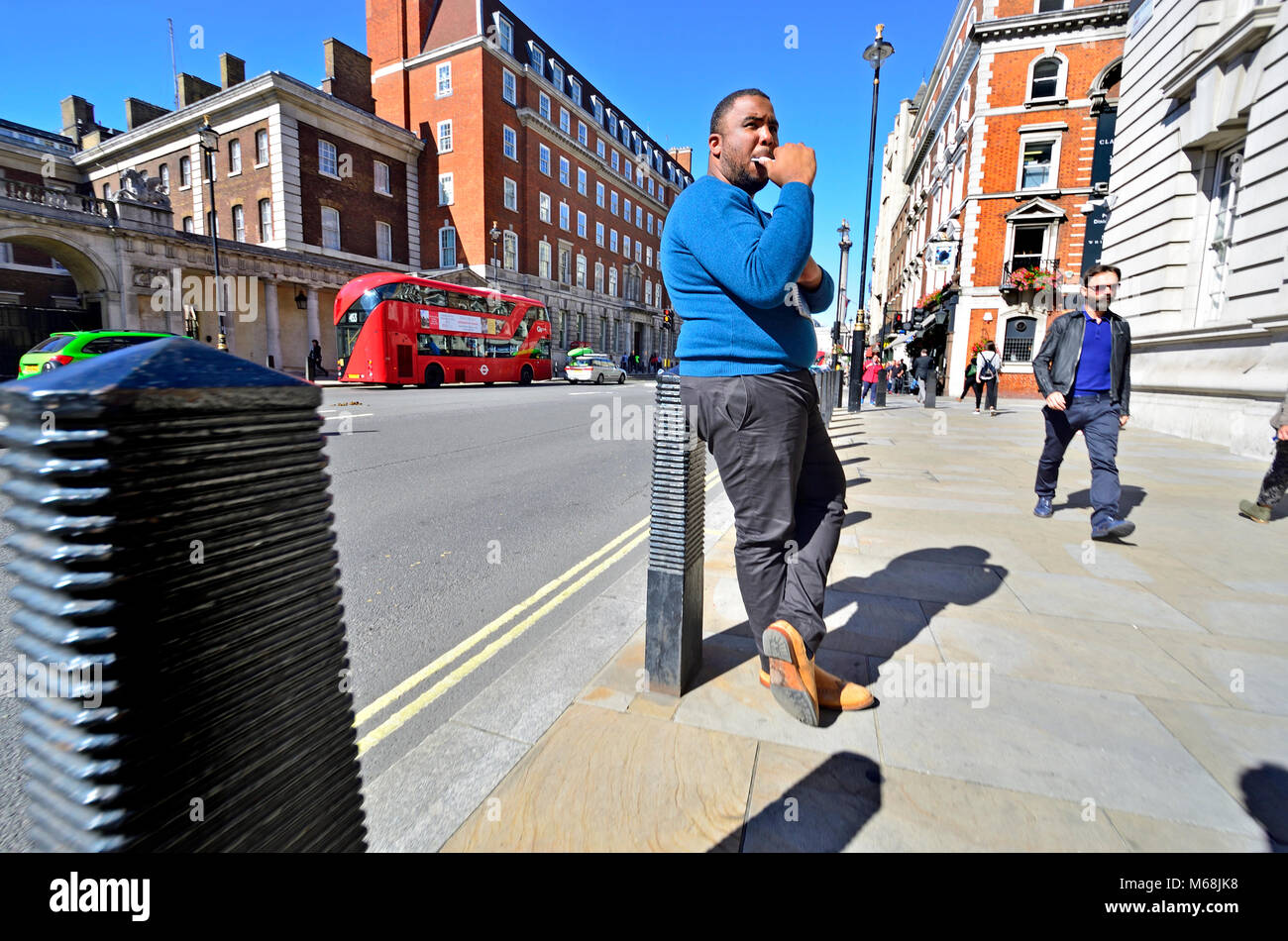Londra, Inghilterra, Regno Unito. Uomo in piedi di Whitehall, apparentemente a mangiare il suo telefono cellulare. Red London bus dietro Foto Stock