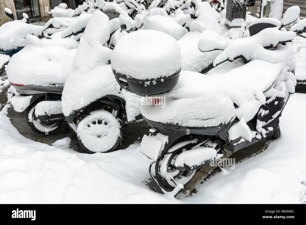Coperta di neve a due e a tre ruote scooter con top casi parcheggiato all'aperto per le strade di Parigi in un giorno d'inverno. Foto Stock
