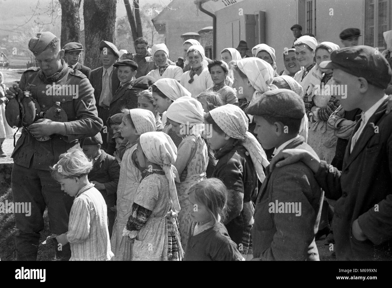 La popolazione locale a guardare i soldati tedeschi di acqua di riempimento di bottiglie in Iugoslavia nell'aprile 1941 durante il WW2 invasione tedesca della Jugoslavia. Foto Stock