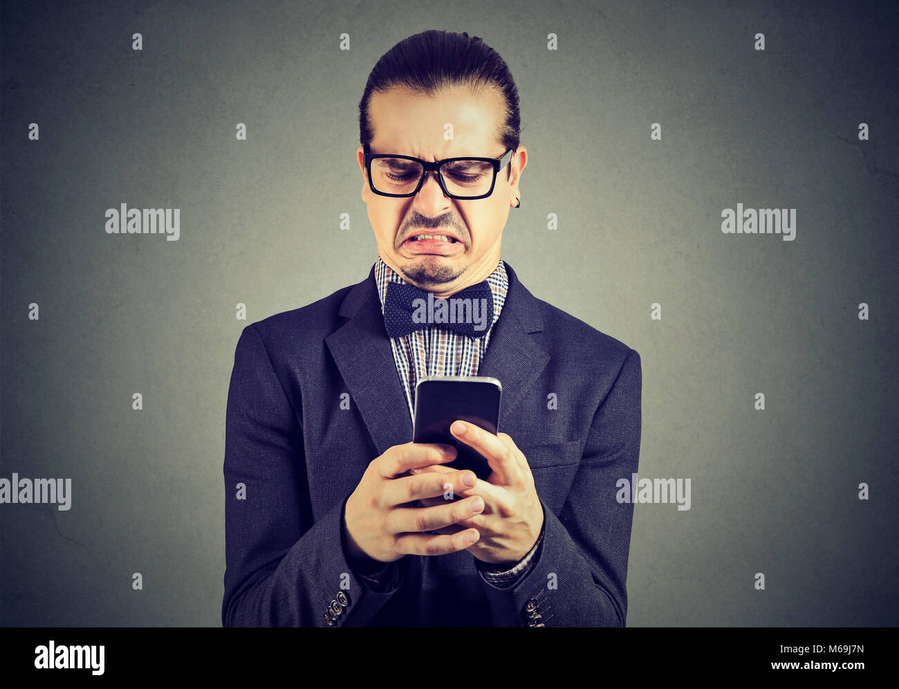 Giovane uomo formale in bicchieri e tuta surf smartphone con sentimento di disgusto essendo offeso. Foto Stock