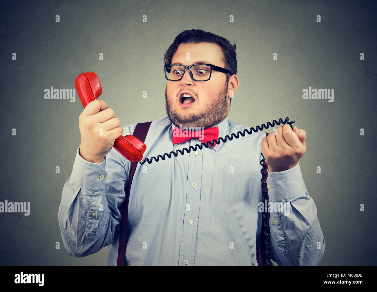 Giovane uomo chunky tenendo il ricevitore del telefono e guardando estremamente sconvolti con comportamenti inappropriati. Foto Stock