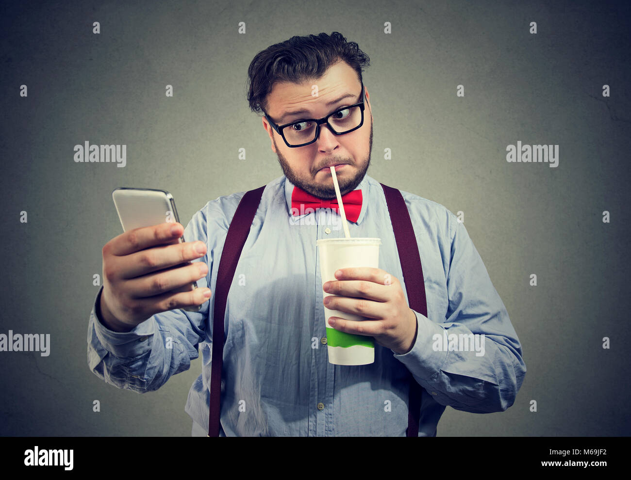 Giovane uomo paffuto addicted to social media e rete tramite telefono e bere soda dolce. Foto Stock
