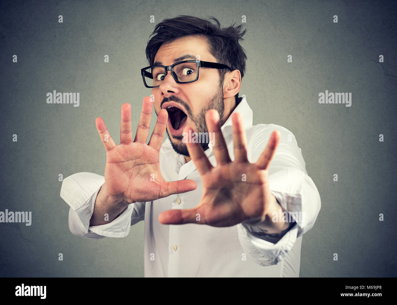Giovani paura l'Uomo in camicia tenendo le mani davanti al viso e urlando in preda al panico. Foto Stock
