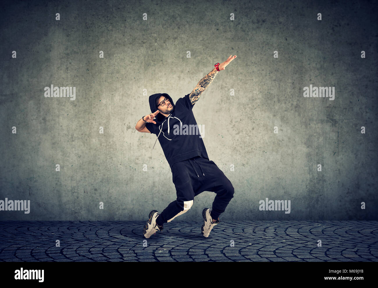 Elegante giovane uomo nel quartiere alla moda di abbigliamento sportivo di eseguire street dance con espressione su sfondo grigio. Foto Stock