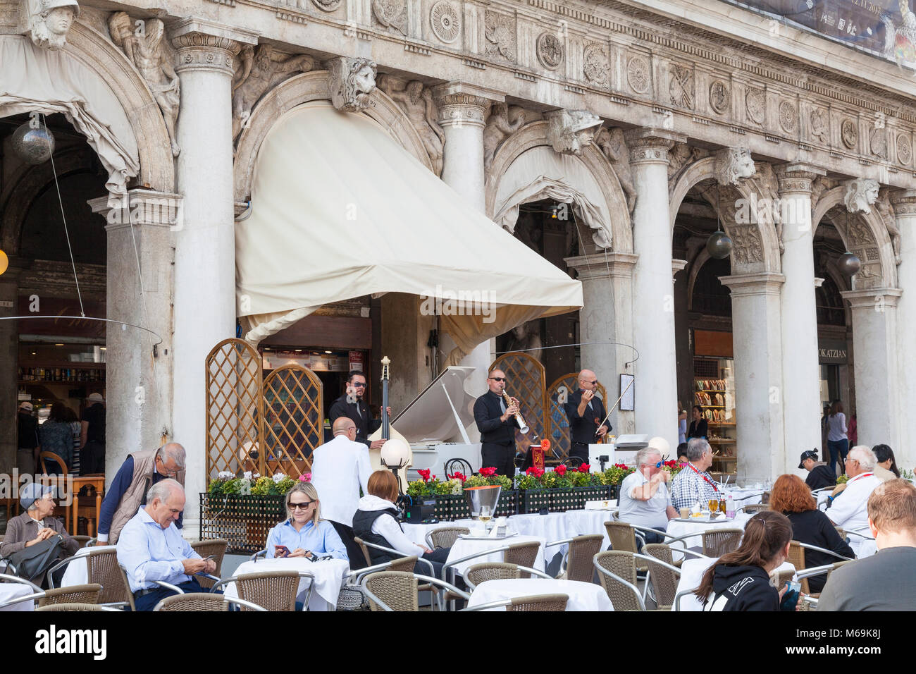Musicisti di suonare musica classica al di fuori del Caffe Chioggia in Piazza San Marco, Venezia, Italia come turisti sedersi al tavolo gustando l'autunno suns Foto Stock