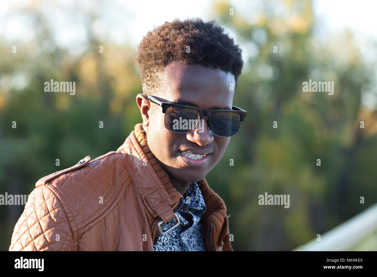 Un bel giovane uomo nero in occhiali da sole e una giacca di pelle su una giornata di caduta Foto Stock