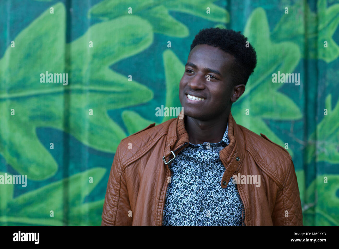 Bel giovane uomo nero sorrisi nella parte anteriore della parete dipinta con foglie Foto Stock