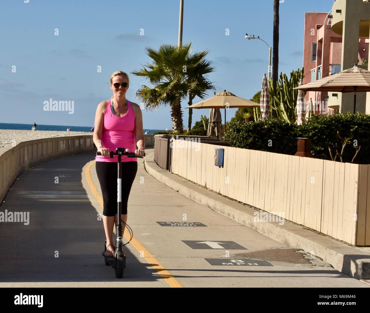 La donna a cavallo di uccello tutto-scooter elettrico lungo la popolare spiaggia lastricata boardwalk in Mission Beach, San Diego, California, Stati Uniti d'America Foto Stock