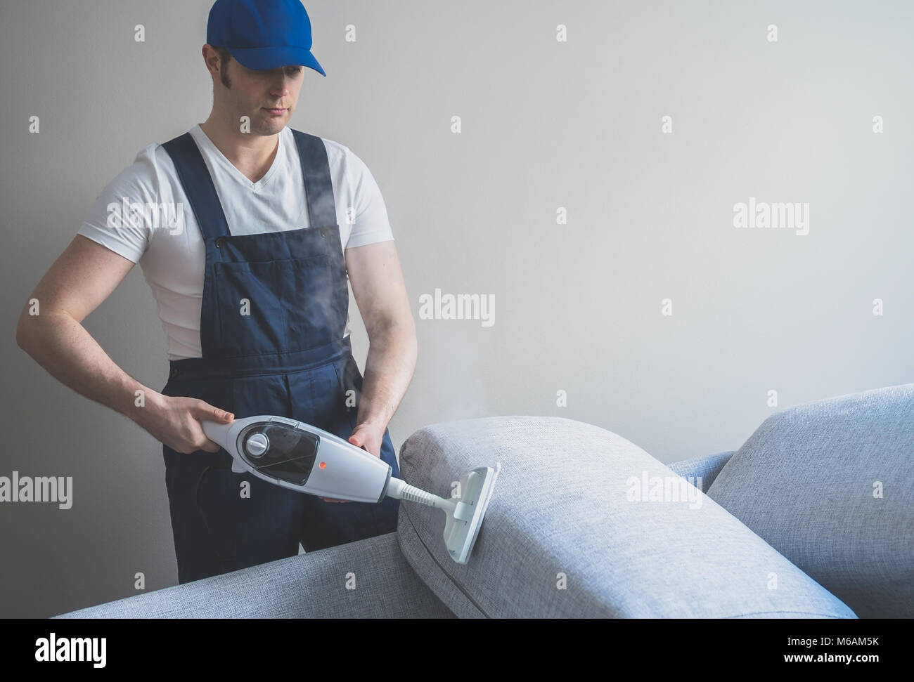 Uomo in uniforme divano di pulizia a secco con un pulitore a vapore. Posto per il testo. Foto Stock