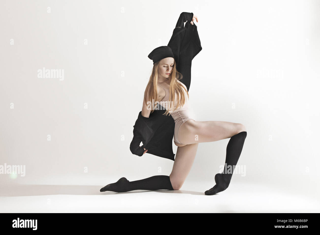 Giovane bellissima ballerina in costume da bagno beige danza su sfondo grigio Foto Stock