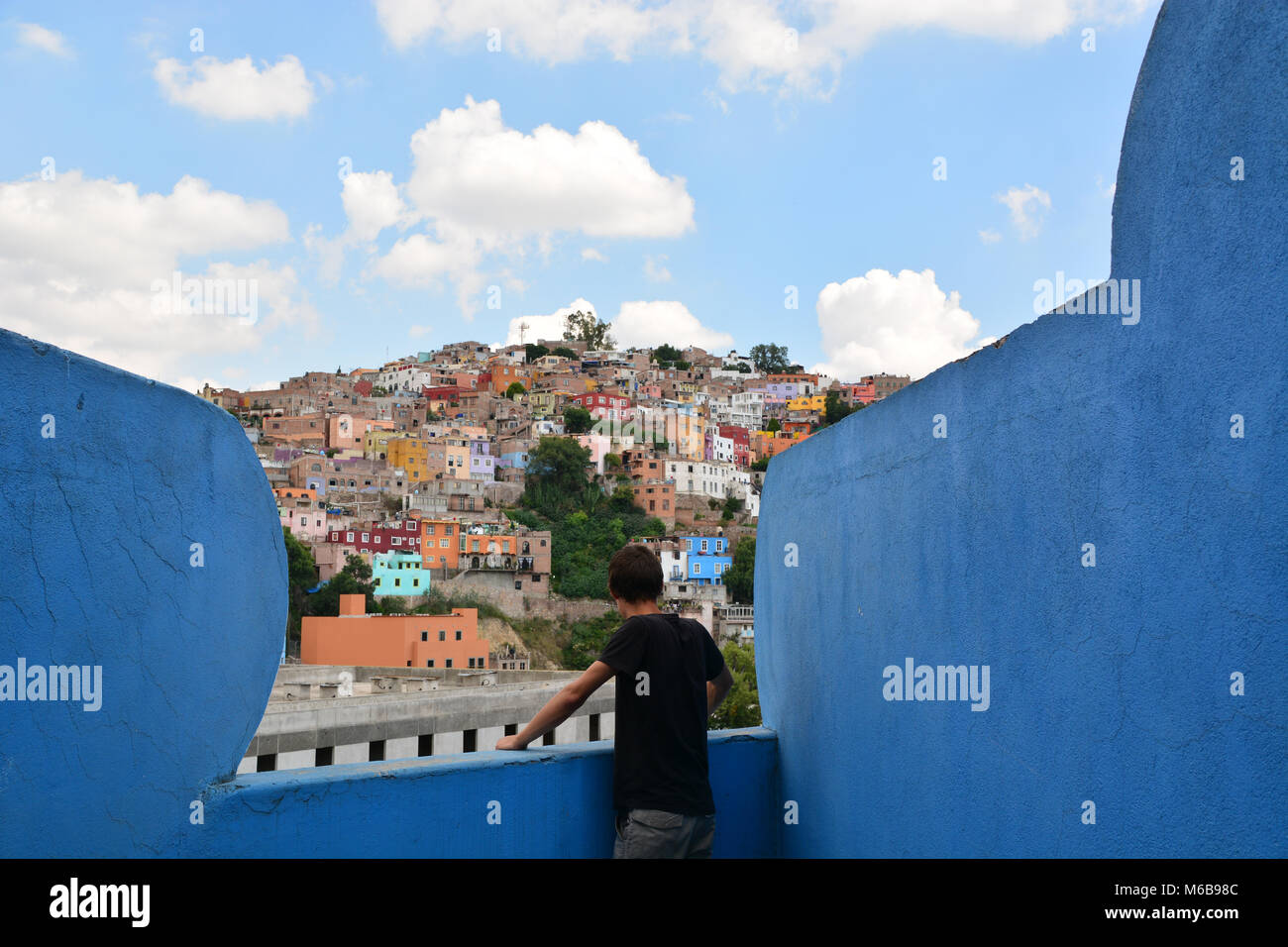 Giovane uomo che guarda oltre il colorato paesaggio di Guanajuato, Messico, da un dipinto di blu, weirdly balcone a. Foto Stock