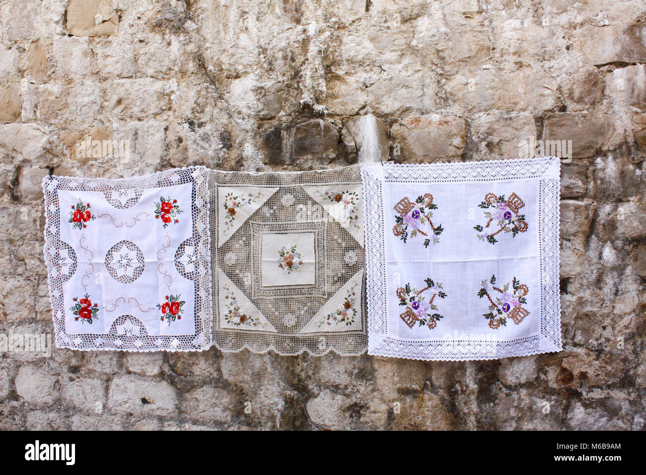 Maglia tradizionale tablewear bianco con motivi floreali che vengono presentati su un vecchio muro di pietra a Dubrovnik, Croazia. Foto Stock