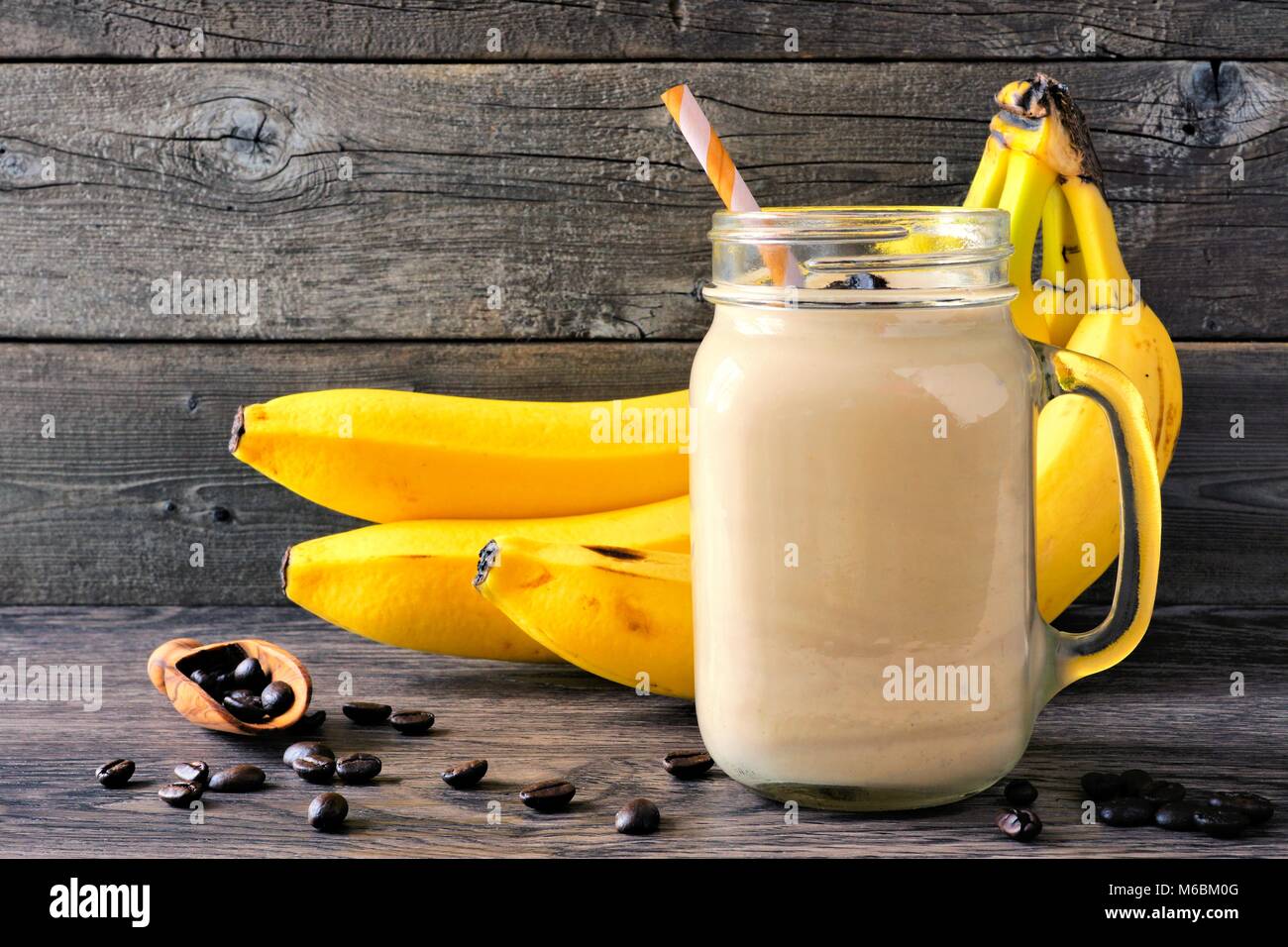 Caffè, frullato di banane in un mason jar con i chicchi di caffè e banane in background. Vista laterale contro un legno rustico sfondo. Foto Stock