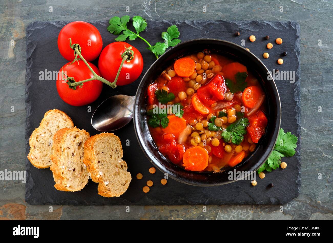 In casa di pomodoro, zuppa di lenticchie, overhead scena, laici piatta al buio su un sfondo di ardesia Foto Stock