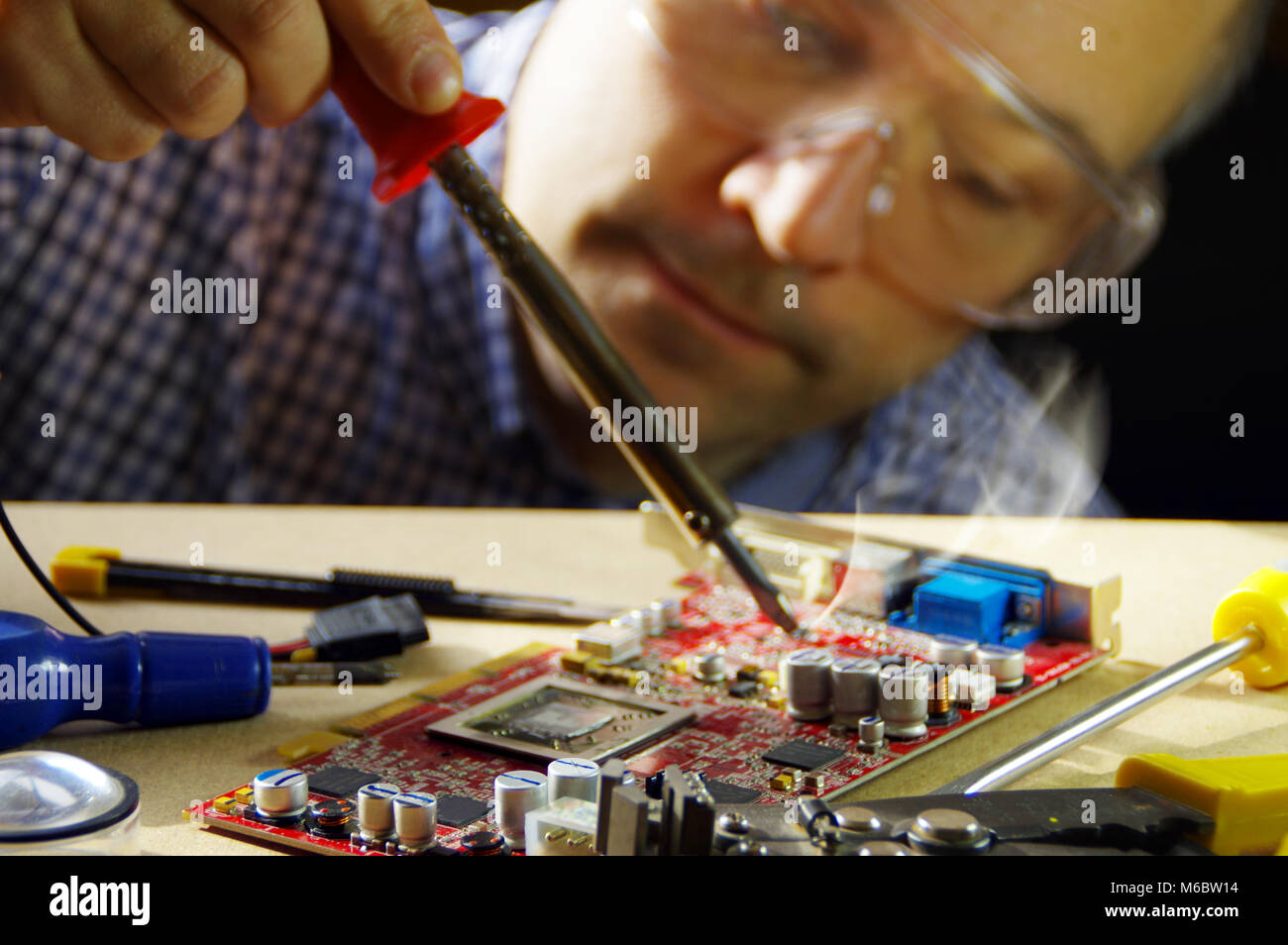 Un uomo al lavoro usando un ferro da saldatore. Il tecnico incentrato sulla riparazione di apparecchiature elettroniche. Foto Stock