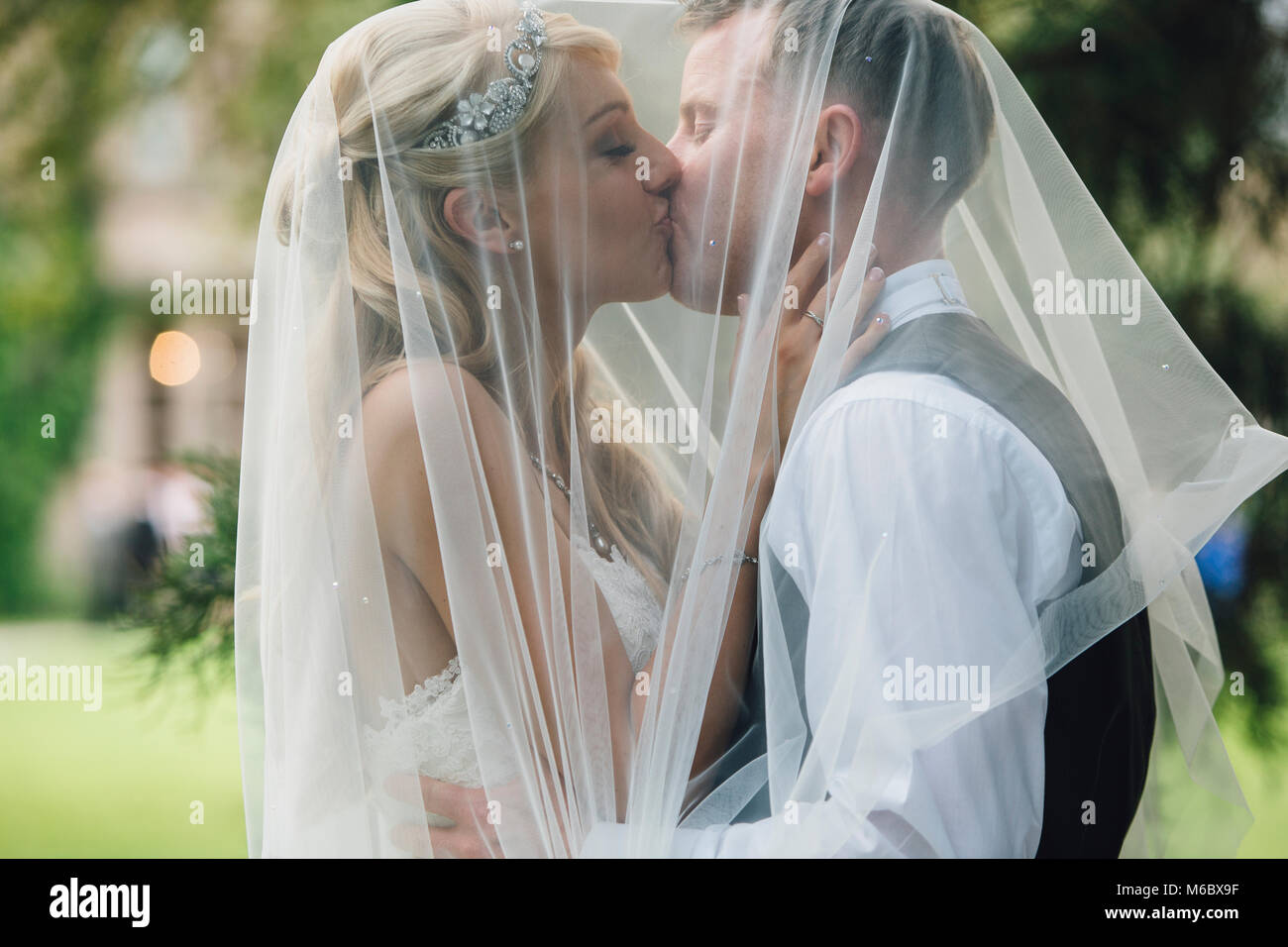 Coppia di novelli sposi stanno abbracciando in un bacio, sotto il velo di spose. Foto Stock